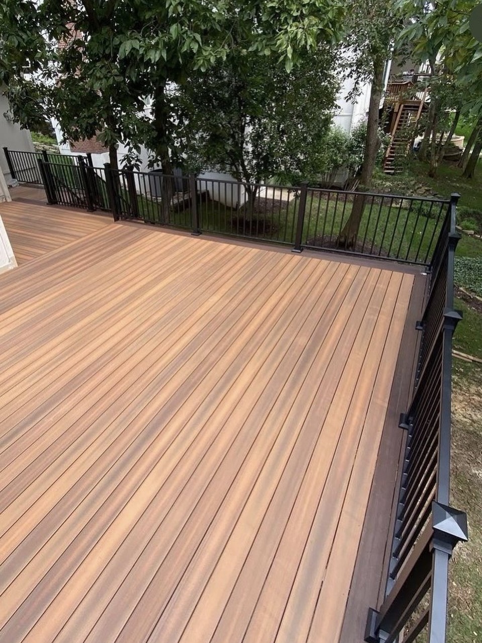 Completed wood-tone composite deck with black metal railing under mature trees in Centreville, Virginia