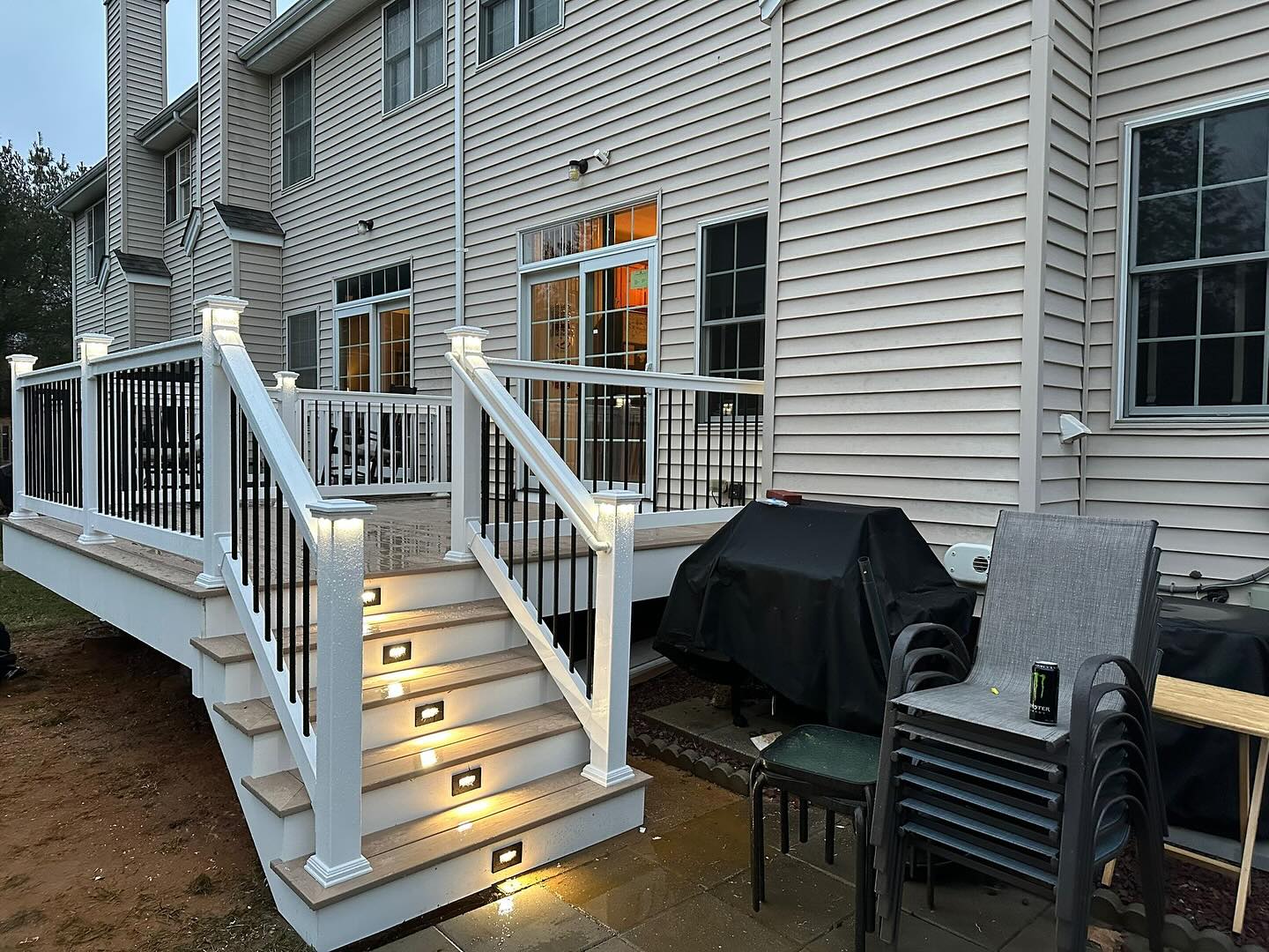 Completed deck with white railing and lighted steps down to a paver patio in Burke, Virginia