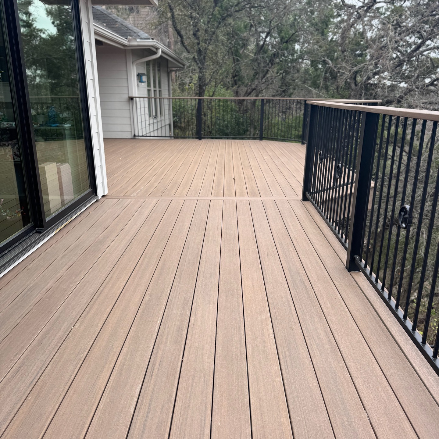 Completed tan composite deck walkway with black metal railing beside the house